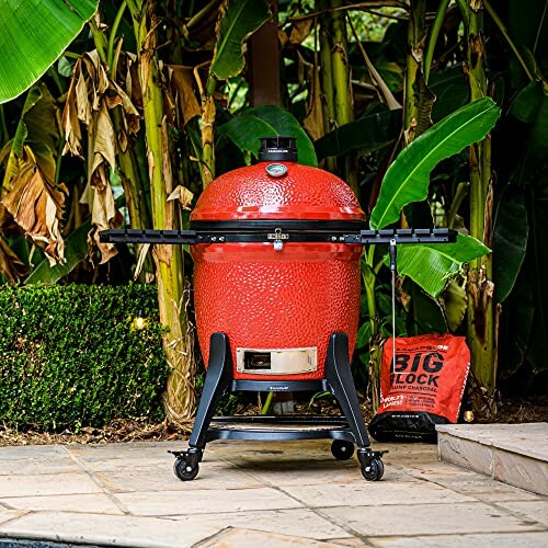 Red kamado grill on wheels in a garden setting