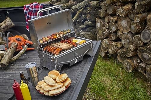 Portable grill with food, buns, and condiments near stacked logs.