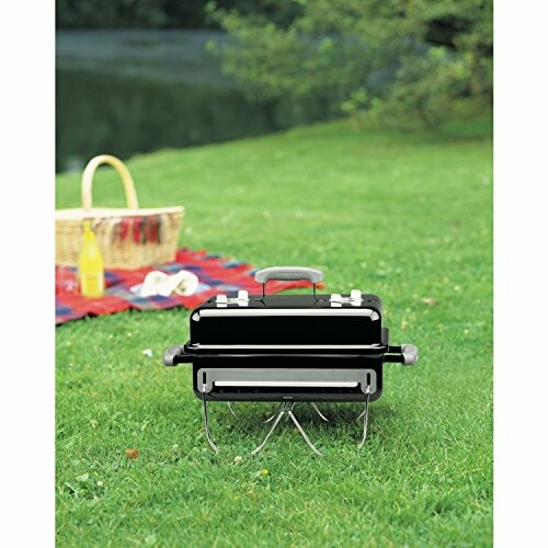 Portable grill on grass with picnic setup.